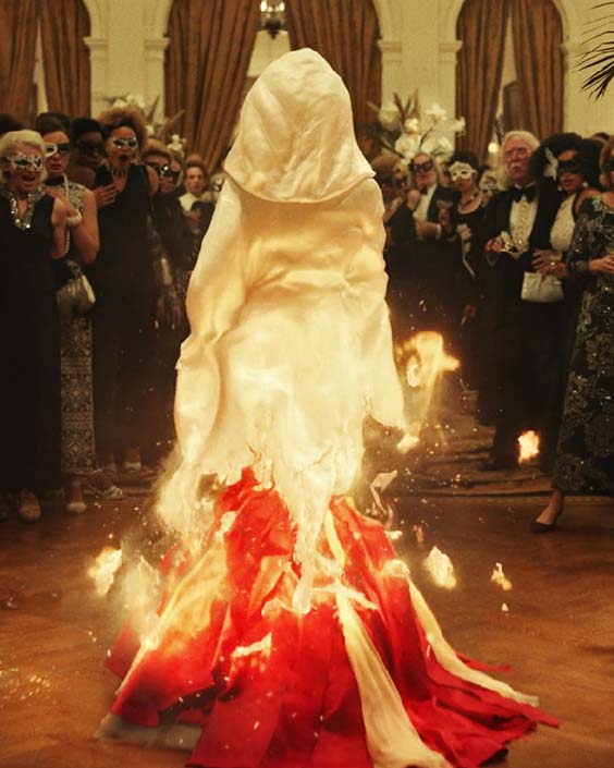 Cruella Estella in a red dress with white cape on fire